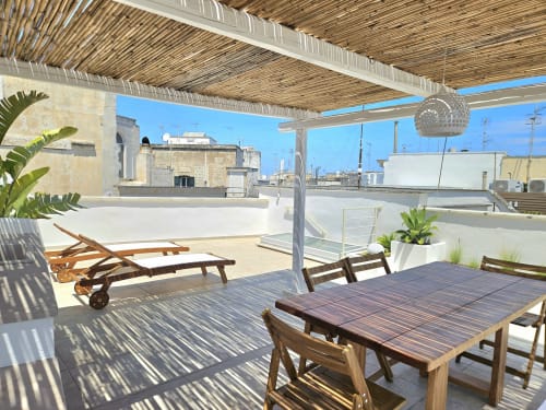 Soleggiata terrazza sul tetto di Pura Vita Apartments a Monopoli con tavolo da pranzo, sdraio e vista sulla città