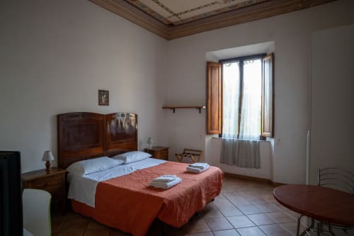 Luminosa camera da letto a Casa di Alfredo B&B a Siena con testata in legno, coperta rossa e finestre con vista sui monumenti