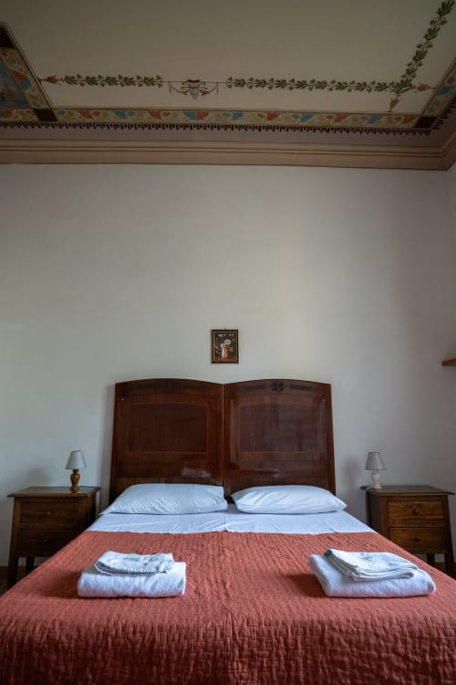 Elegante camera da letto presso Casa di Alfredo a Siena con letto in legno, cuscini bianchi, trapunta rossa e cornici decorative al soffitto