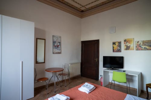 Camera luminosa a Casa di Alfredo a Siena con letto rosso, scrivania, TV e arredi in legno