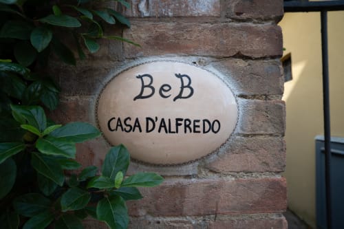 Insegna d'ingresso della Casa d'Alfredo B&B su muro in laterizio con edera verde, Siena Italia