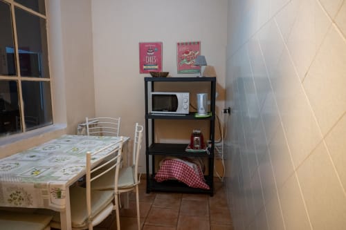 Piccola zona cucina con tavolo da pranzo, scaffali neri con microonde e stoffa a quadri rossi nella camera di Casa di Alfredo B&B