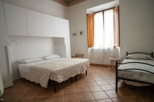 Ampia camera tripla a Casa di Alfredo, Siena con due letti, armadi bianchi, pavimenti in cotto e finestre con vista