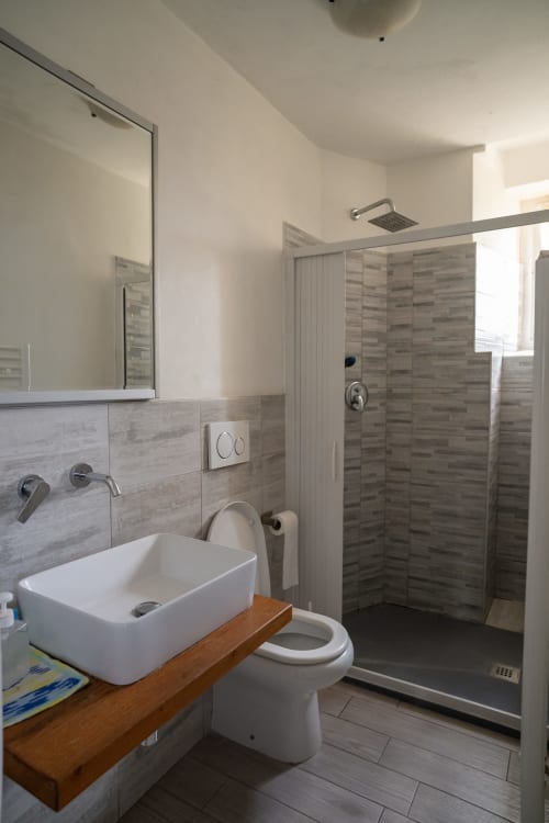 Bagno moderno e condiviso a Casa di Alfredo a Siena con lavabo bianco, toilet e doccia a pioggia con accenti in piastrelle grigie