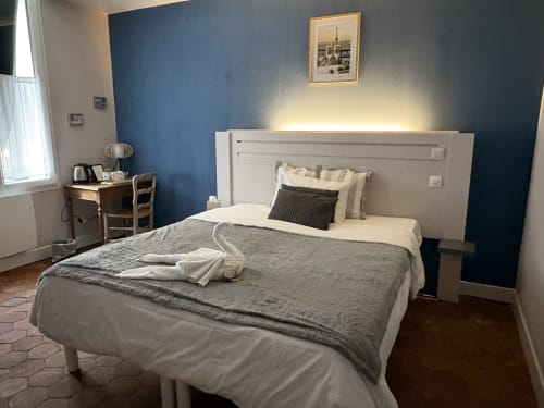 Suite Gustave Flaubert à l'Au Richebourg Nogent, chambre avec mur d'accent bleu, lit blanc, bureau et vue sur la ville