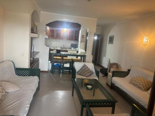 Sala de estar integrada no apartamento de Albufeira com sofá, mesa de refeições, kitchenette e vista para o jardim