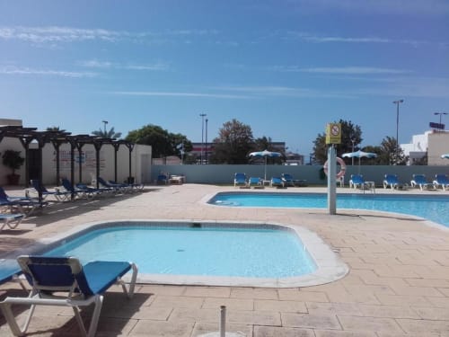 Área de piscina da Albufeira Inn com espreguiçadeiras, guarda-sol e terraço com vista para águas azuis e palmeiras