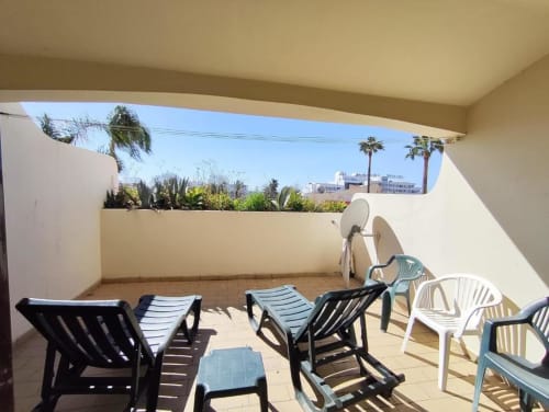 Terraço ensolarado na Albufeira Inn com espreguiçadeiras, cadeiras de refeição, antena parabólica e vista de jardim com palmeiras e edifícios da cidade