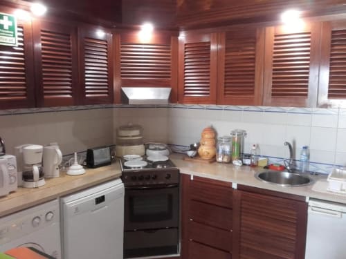 Cozinha moderna em apartamento em Albufeira com armários de madeira, fogão, máquina de lavar louça, cafeteira e pia com vista para o jardim