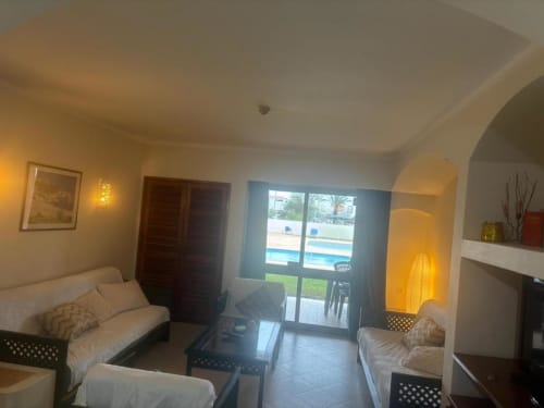 Sala luminosa com sofás creme, vista para piscina através de portas de vidro, iluminação aconchegante e mobiliário moderno no Albufeira Inn