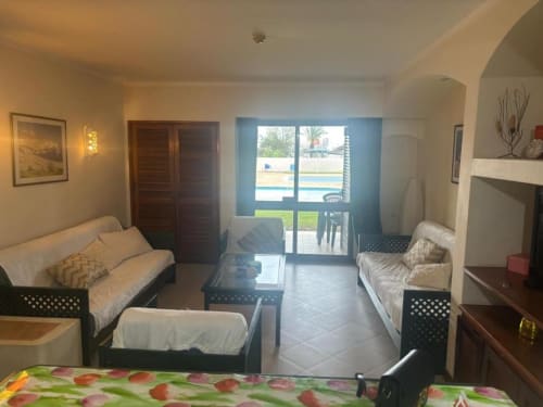 Sala de estar clara em apartamento de Albufeira com sofá, mesa de jantar, camas gêmeas, kitchenette e vista para o jardim