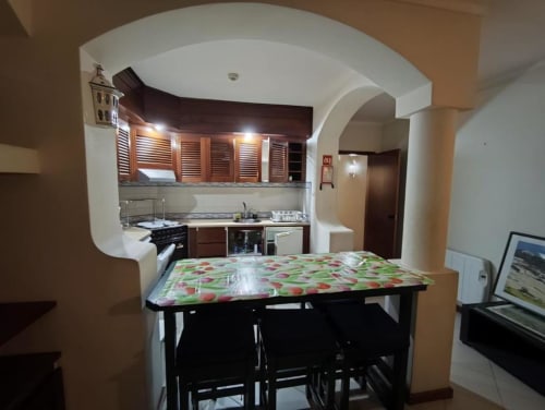 Cozinha e sala de jantar integradas no apartamento em Albufeira com móveis de madeira, mesa de refeições e eletrodomésticos modernos