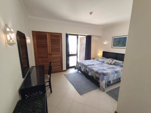 Quarto espaçoso na Albufeira Inn com cama de casal, TV, guarda-roupas em madeira e portas com vista para o jardim