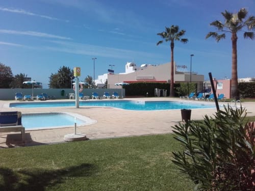 Piscina do Albufeira Inn com espreguiçadeiras azuis, palmeiras e edifício branco sob o sol do Algarve