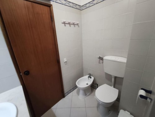 Banheiro limpo com azulejos brancos nas paredes, vaso sanitário, bidê e pia no apartamento Albufeira Inn em Portugal