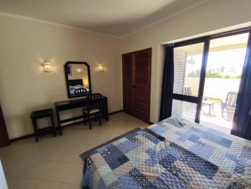 Quarto espaçoso na Albufeira Inn com cama de casal, penteadeira, espelho, arandelas de parede, portas em madeira escura e acesso ao terraço