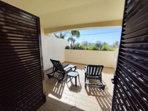 Terraço ensolarado da Albufeira Inn com duas espreguiçadeiras, mesinha e vista para o jardim além da área do pátio