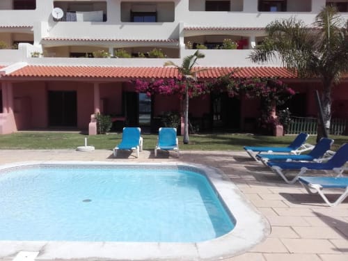 Piscina com espreguiçadeiras azuis na Albufeira Inn, vista para apartamentos em tons de borgonha com buganvílias