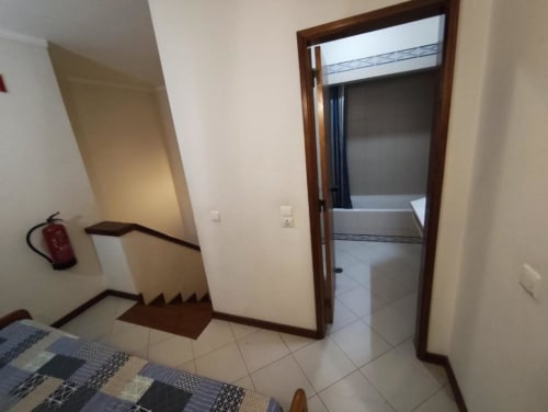 Escada e entrada de hall no apartamento Albufeira Inn com piso em azulejo, corrimão de madeira e porta para quarto