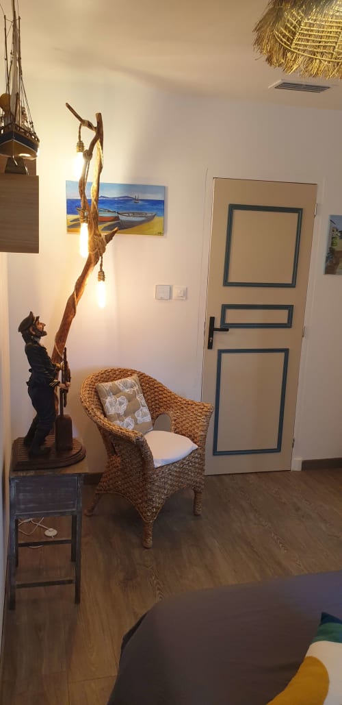Chambre chaleureuse de l'hôtel Vesta Gaia à Saint-Gilles avec fauteuil tressé, lampadaire en bois flotté et décoration côtière