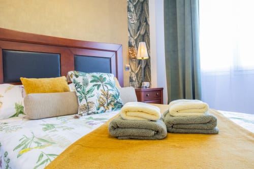 Dormitorio de apartamento Haus Holiday Homes con toallas dobladas en la cama, ropa de cama tropical y cortinas con vista a la piscina en San Pedro del
