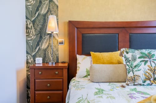 Dormitorio con mesilla de madera, papel tapiz de hojas tropicales y ropa de cama floral en Haus Holiday Homes, San Pedro del Pinatar