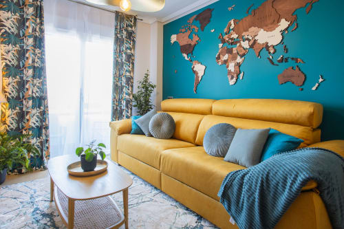 Sala de estar moderna en San Pedro del Pinatar con sofá mostaza, pared azul verdoso, mapa mundial y decoración botánica