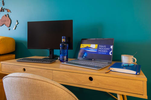 Espacio de trabajo moderno en Haus Holiday Homes con doble monitor, laptop y accesorios de escritorio frente a pared turquesa