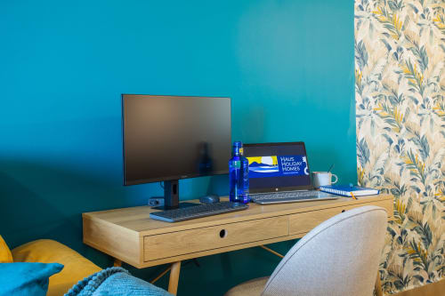 Espacio de trabajo moderno en Haus Holiday Homes con monitor de escritorio, laptop y acentos azules sobre pared turquesa