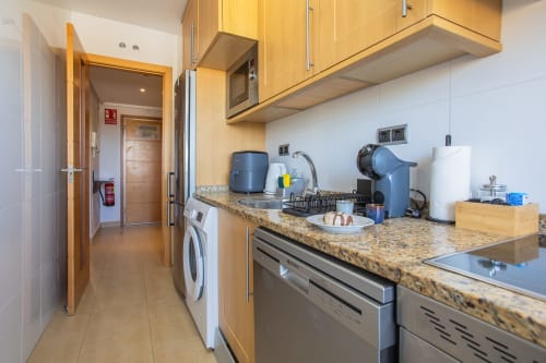 Cocina moderna con encimera de granito, armarios de madera, electrodomésticos de acero inoxidable y lavadora en apartamento