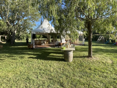 Chapiteau blanc dressé sur la pelouse verte des Jardins Du Soleil à Avignon, avec saules pleureurs et table tonneau rustique