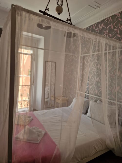 Elegant canopy bed with sheer curtains in Zuni Guest House Lisboa bedroom, city view through balcony doors