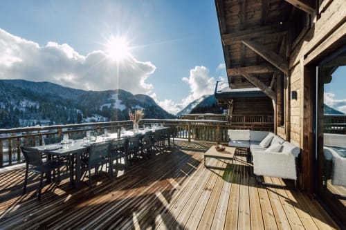 Terrasse ensoleillée du chalet montagnard Altitudia Les Gets avec table à manger, espace détente et pics alpins enneigés