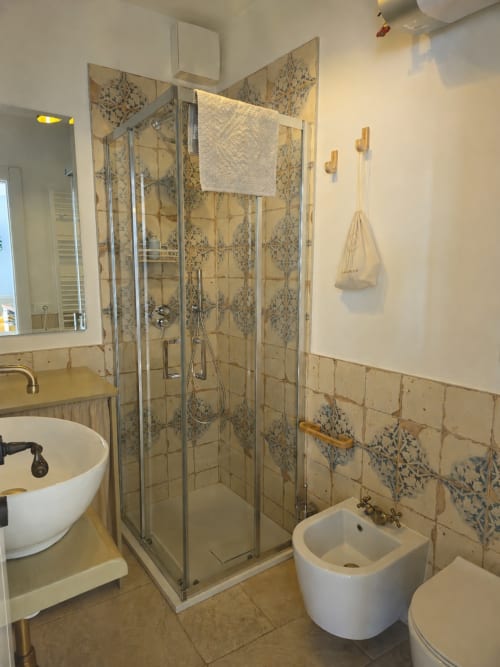 Modern bathroom in Pura Vita Apartments, Monopoli with glass shower, white fixtures and decorative blue floral tiles