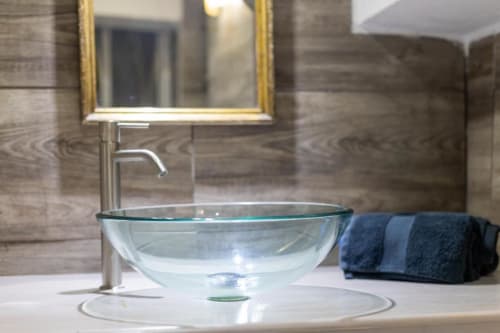 Elegante lavabo in vetro con rubinetto cromato, specchio dorato e asciugamani piegati nel lussuoso bagno spa di Palermo