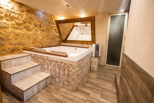 Lussuosa spa del bagno presso Oltre Exclusive & Caveau a Palermo con vasca idromassaggio incassata, pareti in pietra, gradini in legno