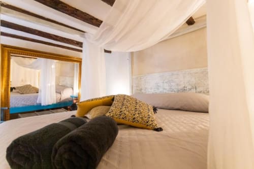 Suite lussuosa a Palermo con letto a baldacchino, travi in legno, cuscini decorativi e specchio dorato riflettente eleganza