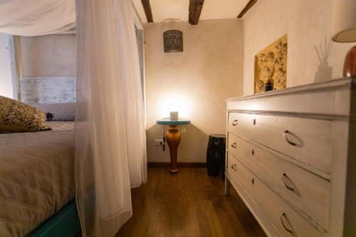Elegante camera da letto presso l'Oltre Exclusive Caveau di Palermo con letto a baldacchino, cassettiera bianca, pavimenti in legno e illuminazione d'atmosfera