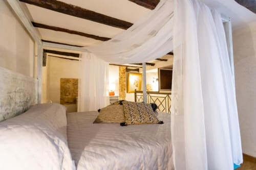 Camera da letto lussuosa con drappi sheer bianchi, soffitto con travi in legno e accesso al balcone presso Oltre Exclusive a Palermo.