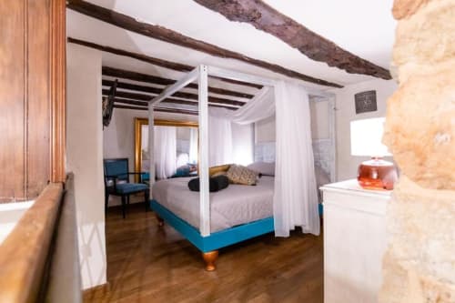 Lussuoso letto a baldacchino con tende bianche in camera d'hotel boutique a Palermo con travi a vista e muri in pietra