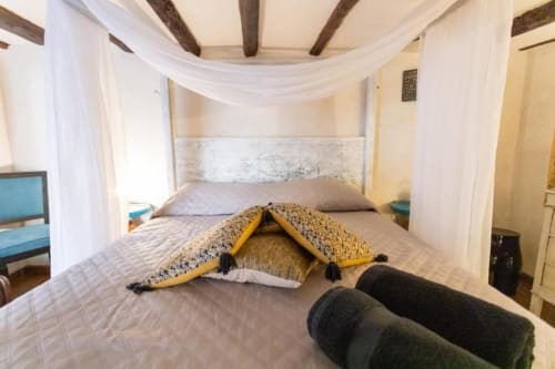 Camera da letto lussuosa con letto a baldacchino, cuscini decorativi, travi a vista e plaid giallo presso l'Oltre Exclusive di Palermo