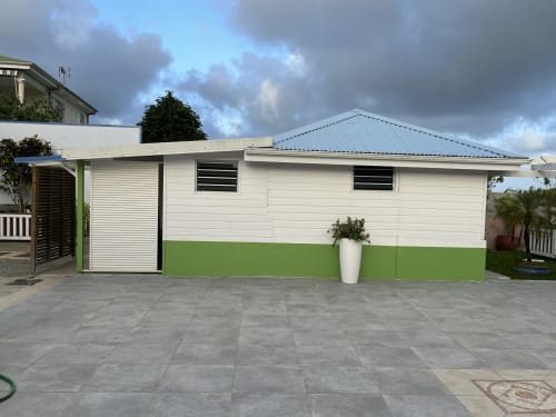 Bungalow d'hôtes Résidence B&L Lagon à Sainte-Luce, façade blanc et vert, toit métallique et cour pavée