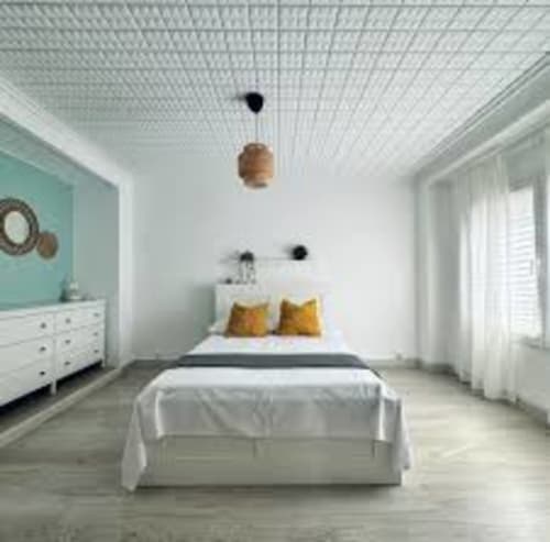 Modern apartment bedroom in Ruzafa, Valencia with white bed, yellow pillows, turquoise accent wall, and natural light from