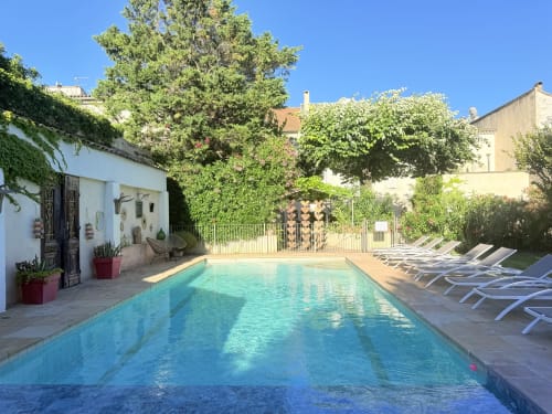 Rectangular pool with loungers at Hôtel La Suite in Villeneuve-lès-Avignon, surrounded by lush greenery
