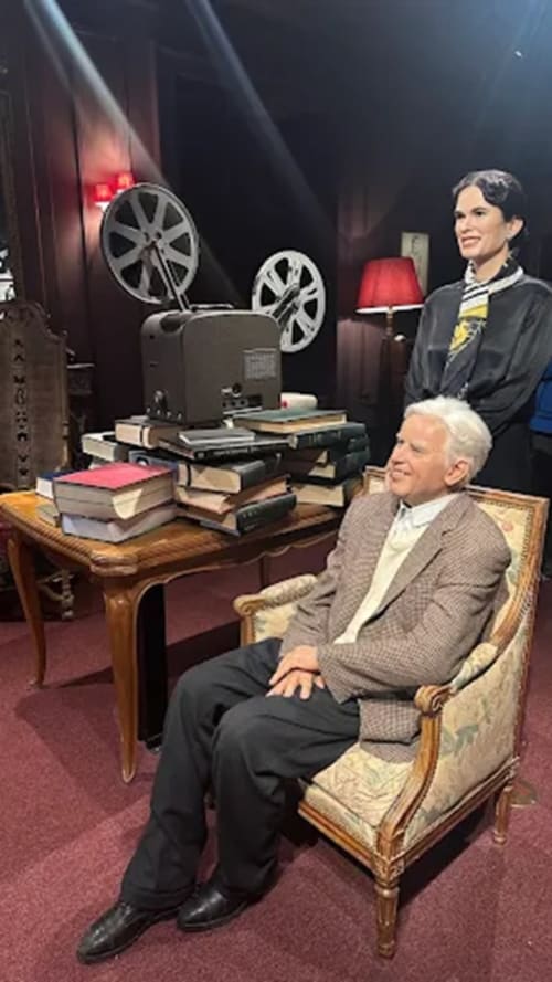 Man and woman in vintage cinema setting at Hôtel Les Triolets, Châtel with film projector and books on desk