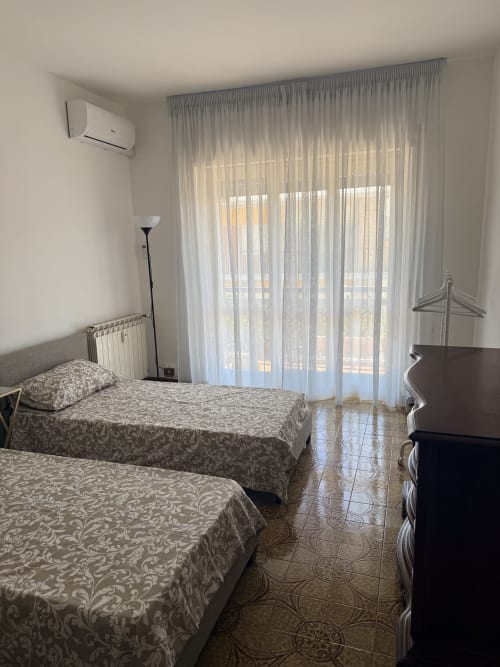 Bright twin bedroom with city view at Claudia Apartments Rome, featuring patterned bedspreads, modern AC unit, and sheer