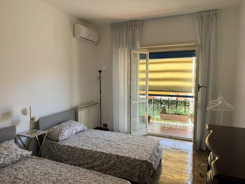 Modern bedroom at Claudia Apartments Rome with twin beds, balcony access, AC unit, and city views