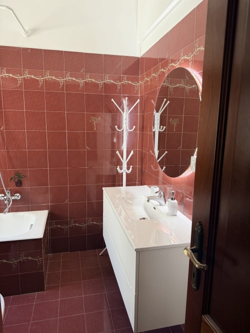 Modern bathroom with red patterned tiles, white sink vanity, round mirror, and white towel rack at Claudia Apartments Rome