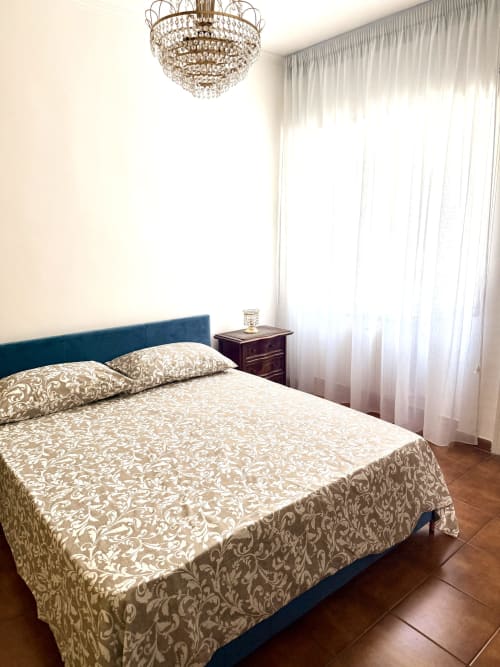 Elegant bedroom at Claudia Apartments Rome with blue headboard, patterned bedding, crystal chandelier, and sheer curtains