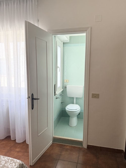 Modern bathroom with white toilet, pedestal sink, and mint green tile walls at Claudia Apartments Rome